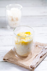 Summer appetizer of Thailand concept. Durian and sticky rice with coconut milk cream in transparent glass on white wooden table and brown table cloth. Famous street food in Thailand.