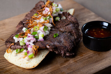 Juicy meat chop with different types of onions and red sauce on a baguette on a wooden board
