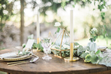 Gold and pastel wedding dinning table decoration. Geometic shapes, rustic decor, eucalyptus branches, candles, menu. Bokeh background.