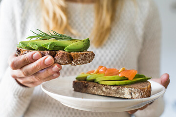 close up of woman holding plate with avocado toast as fresh snack, day light.