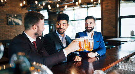 Handsome businessmen are drinking beer, talking and smiling while resting at the pub
