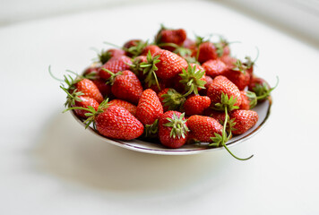 A lot of red, juicy strawberries on a plate. Red berries on a white background. Natural eco-product.