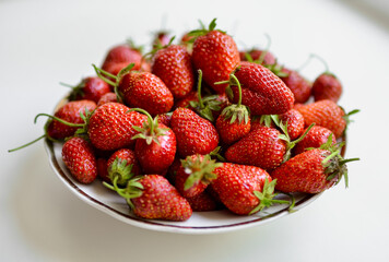 A lot of red, juicy strawberries on a plate. Red berries on a white background. Natural eco-product.