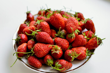 A lot of red, juicy strawberries on a plate. Red berries on a white background. Natural eco-product.
