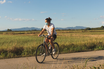 Young man on a bicycle on a country road wearing a mask