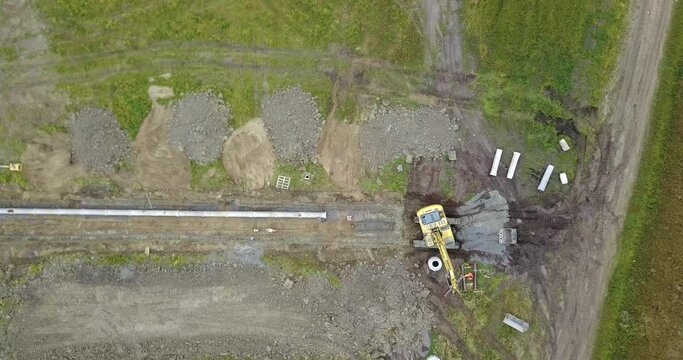 Rotierender Bagger verlegt eine Leitung aus Rohren in einem Baugebiet, Baustelle aus der Vogelperspektive 