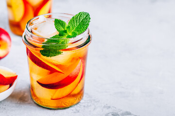 Homemade peach iced tea or lemonade with fresh mint and ice cubes in glass jar