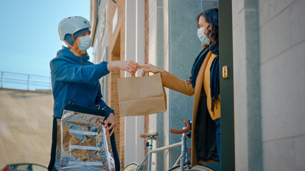 Food Delivery Man Wearing Protective Medical Face Mask and Thermal Backpack on a Bike Delivers...