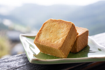Delicious pineapple pastry in a plate for afternoon tea on wooden railing of a teahouse in Taiwan with beautiful landscape in background, close up.