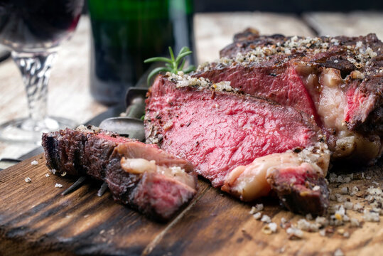 Barbecue dry aged wagyu tomahawk steak with red wine as close-up on a rustic wooden cutting board