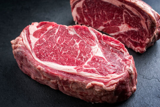 Two raw dry dged Kobe rib-eye steaks as closeup on a black board