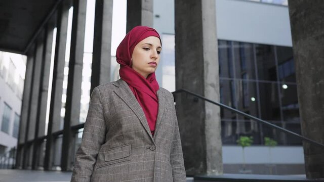 Young beautiful muslim serious woman wearing hijab headscarf walking down stairs near futuristic building. business woman concept.