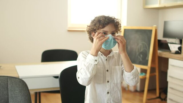 Schoolboy in a classroom is putting on a protective mask. Post quarantine school, new normality, new rules, social distance