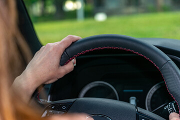 Woman driving car, visible speedometer screen and beautiful natural green scenery.