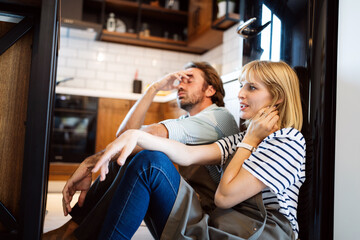 Young happy tired couple sitting on kitchen floor after cooking