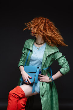girl with red hair and white skin, bows her head, curly curly hair, lush hairstyle, red lipstick, beautiful makeup, green polto and orange long boots