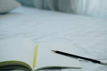 notebook & pencil on white bed mattress