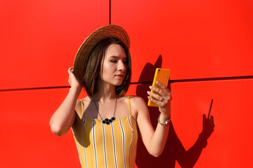 slender girl posing against a red wall with a phone