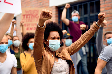 African American woman wearing protective face mask while protesting with arms raised on city streets. - obrazy, fototapety, plakaty