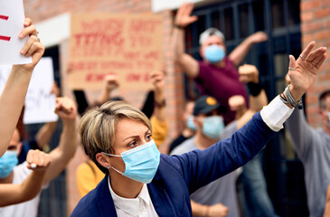 Caucasian woman wearing protective face mask while being with group of protesters on city streets.