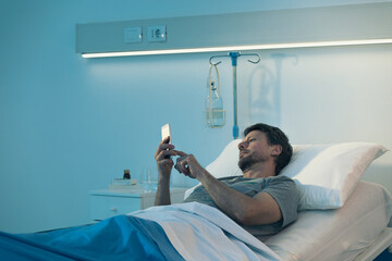 Male patient at the hospital and chatting with smartphone. - 356952963