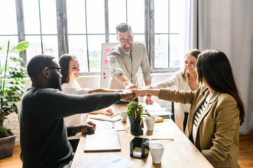 Young creative multiracial team at the office. Their fists stacked together, sign and symbol of...