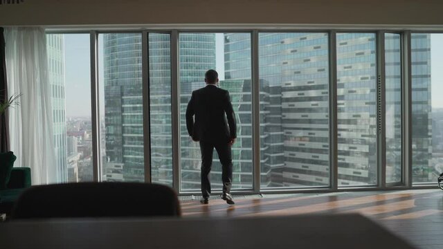 Businessman looking at city through window. Successful businessman on the background of skyscrapers. Businessman in office with expensive interior.