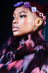 young pretty african american woman in spotted fur coat and flowers jewelry posing on black background