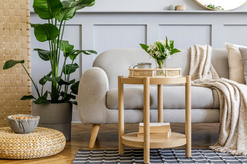 Scandinavian living room interior with design grey sofa, wooden coffee table, tropical plants, shelf, mirror, furniture, plaid pillow, teapot, book and elegant personal accessories in home decor.