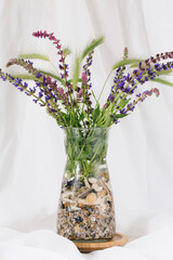 Transparent glass vase with sea shells filled with salvia wild flowers.