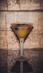 Glazed cocktail glass with a yellow drink and berries