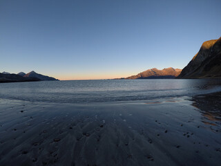 beautiful calm blue waves hitting white frozen sandy beach in late autumn in the arctic circle with deep mountain and open sea view on clear sky background