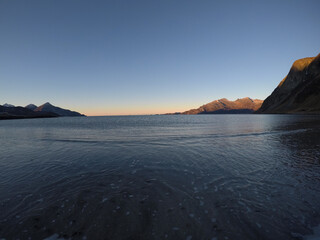beautiful calm blue waves hitting white frozen sandy beach in late autumn in the arctic circle with deep mountain and open sea view on clear sky background