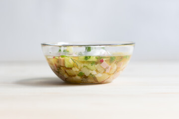 Cold soup okroshka in glass bowl on wooden background