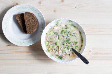 Cold russian soup okroshka with spoon and bread on wooden rustic background, flat lay