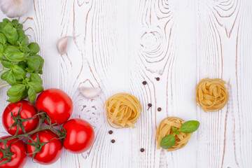 Obraz na płótnie Canvas Top view raw tagliatelle pasta with fresh basil, garlic and tomatoes on a rustic white table, flat lay, copy space.