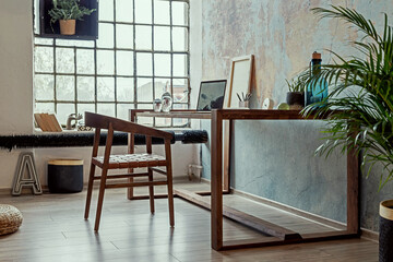 Stylish interior design of office space in loft apartment with wooden desk, chair, office supplies, laptop, plants, lamp and elegant accessories. Modern home office decor. Bright space. Template.