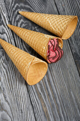 Fototapeta na wymiar Strawberry ice cream in a waffle cone. Garnished with Chocolate. Nearby are empty waffle cones without ice cream. On pine boards painted in black and white.