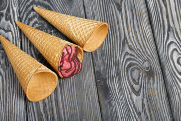 Fototapeta na wymiar Strawberry ice cream in a waffle cone. Garnished with Chocolate. Nearby are empty waffle cones without ice cream. On pine boards painted in black and white.