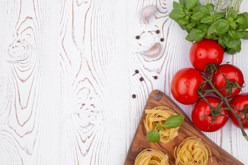 Top view raw tagliatelle pasta with fresh basil, garlic and tomatoes on a rustic white table, flat lay, copy space.
