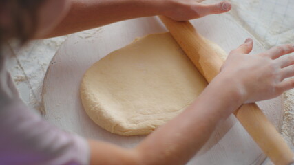 Girl hands rolling dough on table with mother at kitchen. Family cooking at home
