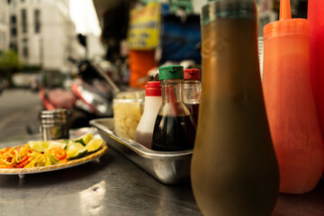 Traditional Vietnamese noodle condiment tray with dish of lemon slices, jar of chili, fish sauce, soy sauce, spoons and chopsticks at street food cart in Ho Chi Minh city, Vietnam