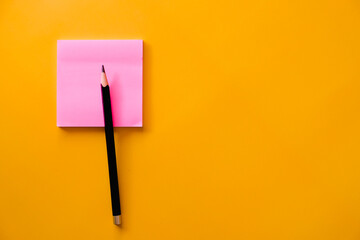Black  pencil and pink note paper on yellow background