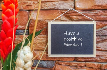 Image of motivational greeting have a positive monday on black mini notice board hanged on brick wall besides partly seen decorative plant. Selective focus on notice board. Others in gradient blur.