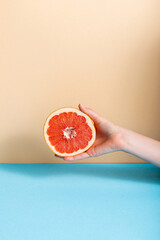 cropped view of female hand with juicy grapefruit half on beige and blue background