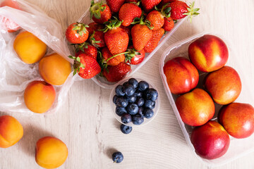 top view of fruit composition with blueberries, strawberries, nectarines and peaches in plastic containers on wooden surface