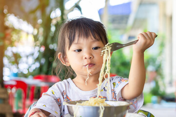 Portrait​ image​ of​ 2-3 years​ old​ of​ baby.​ Happy​ Asian​ child​ girl​ enjoy​ eating​ some​ noodles by​ herself.​ Healthy​ Food​ and​ kid​ concept.