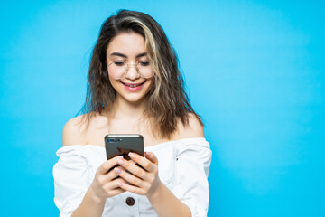Portrait of young smiling woman using mobile phone against blue background