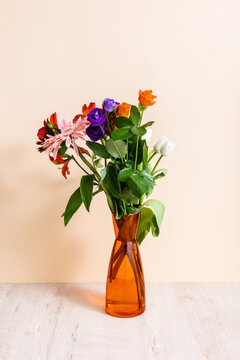 Floral composition with bouquet in orange vase on wooden surface on beige background