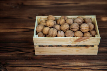Box filled with inshell walnuts on a wooden background. View from above. Natural, healthy product. Space for text.